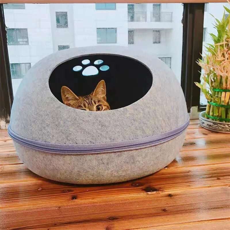 Chat roux regardant hors d'un panier douillet en feutre de laine gris.