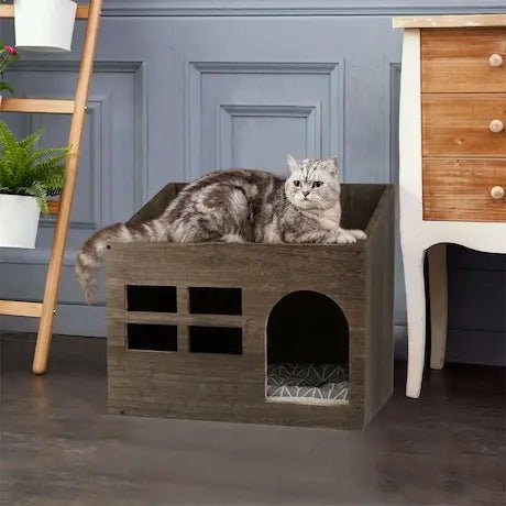 Chat gris tigré se relaxant sur un lit maison en bois design.